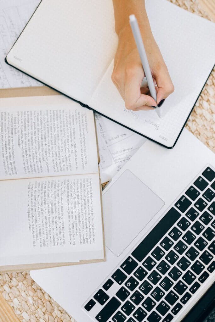 woman writing down in planner near open book and laptop